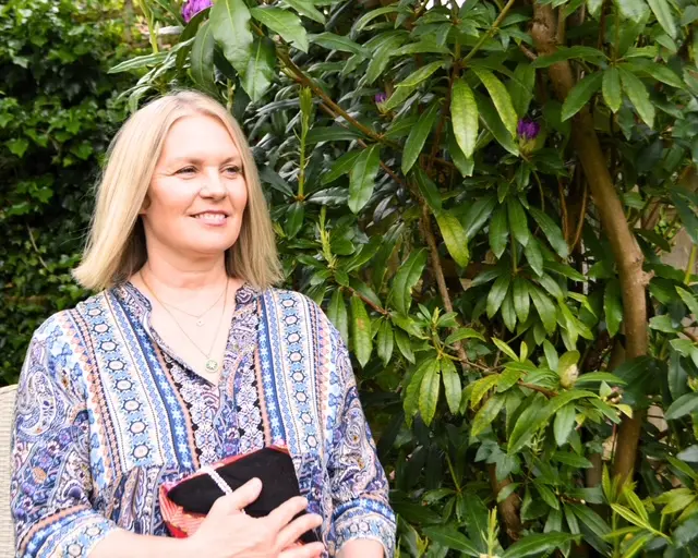 Nicola standing outdoors beside leafy greenery